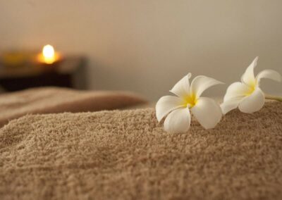 Jolies fleurs blanches posés sur une table de massage, avec une bougie en arrière-plan, symbolisant le bien-être et la paisibilité.