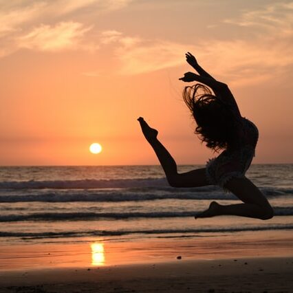 Une jeune femme saute en dansant, devant un beau coucher de soleil sur la plage.