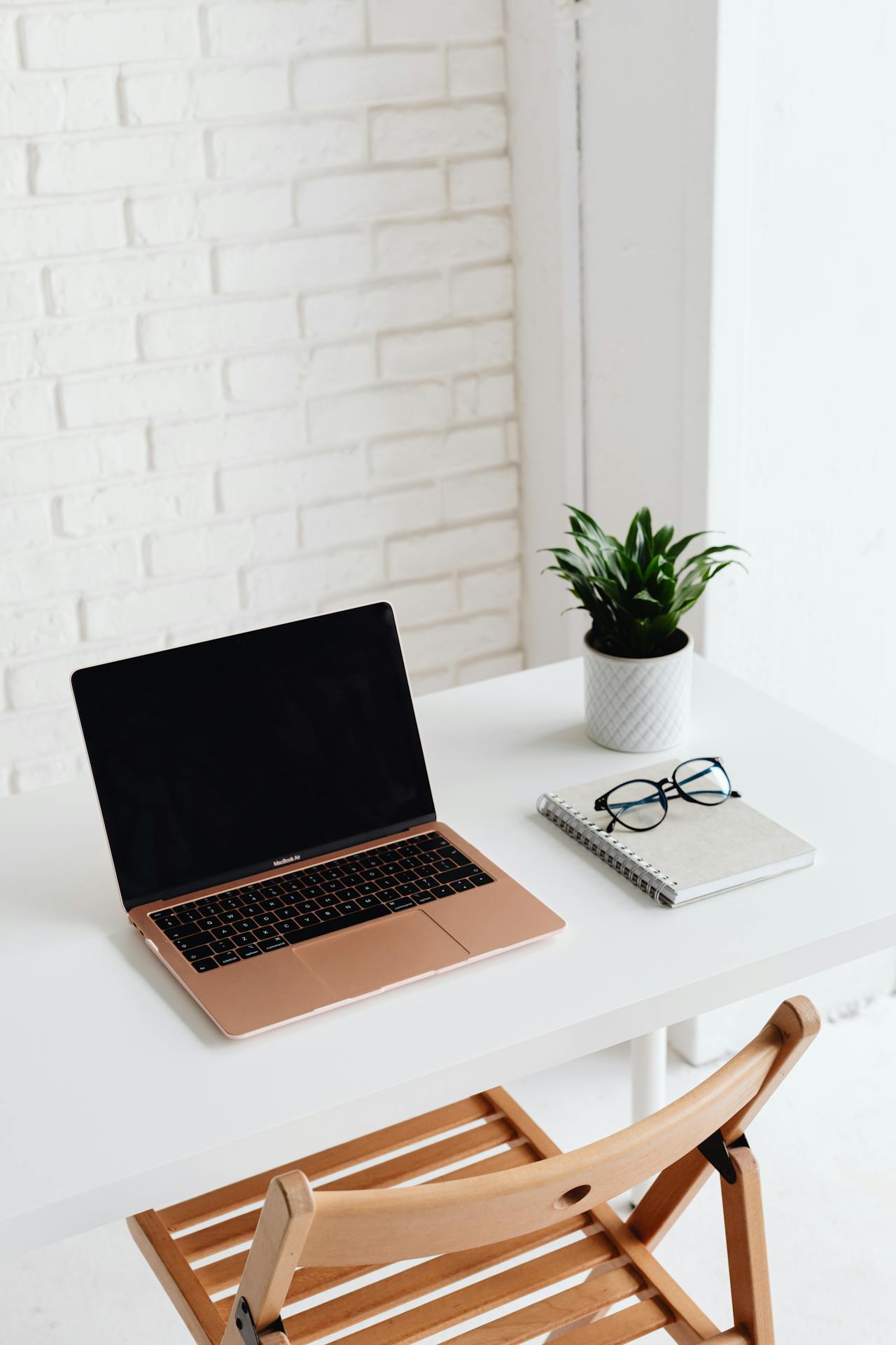 Poste de travail épuré et minimaliste avec un PC portable, un carnet, une paire de lunettes et une petite plante verte, représentant le bien-être et la respiration. 