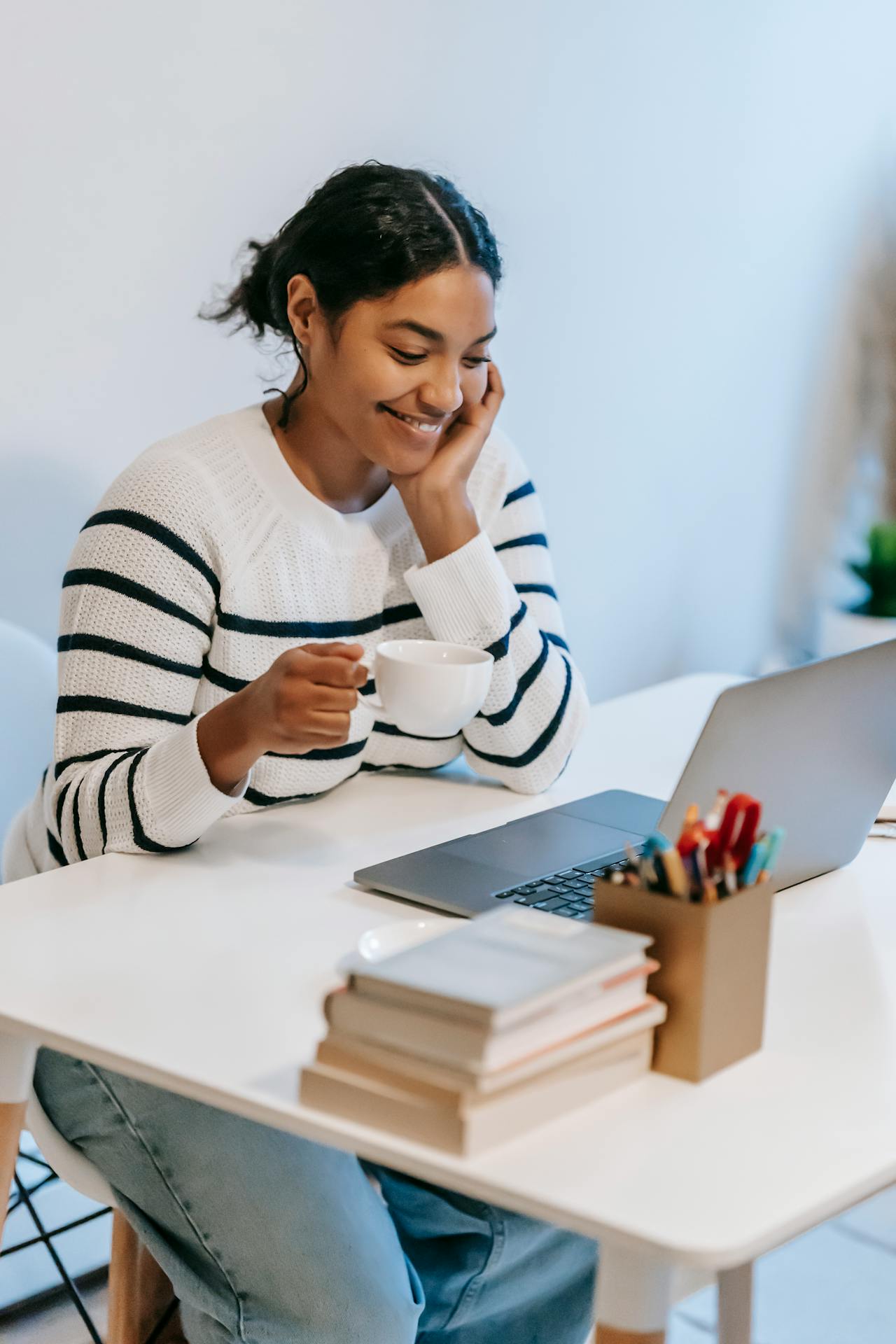 Une jeune femme relit un article de blog sur son PC, avec le sourire et une tasse de thé à la main.