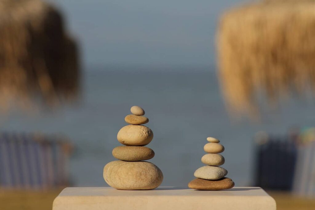 Deux piles de galets beiges de plage posés sur une table devant la mer, en plein été