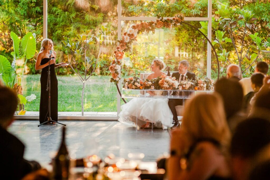 Femme debout faisant un discours de mariage à des mariés assis à leur table