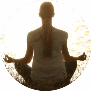 Femme assise devant une mer éclairée par un étincelant coucher de soleil, en pleine séance de yoga méditatif