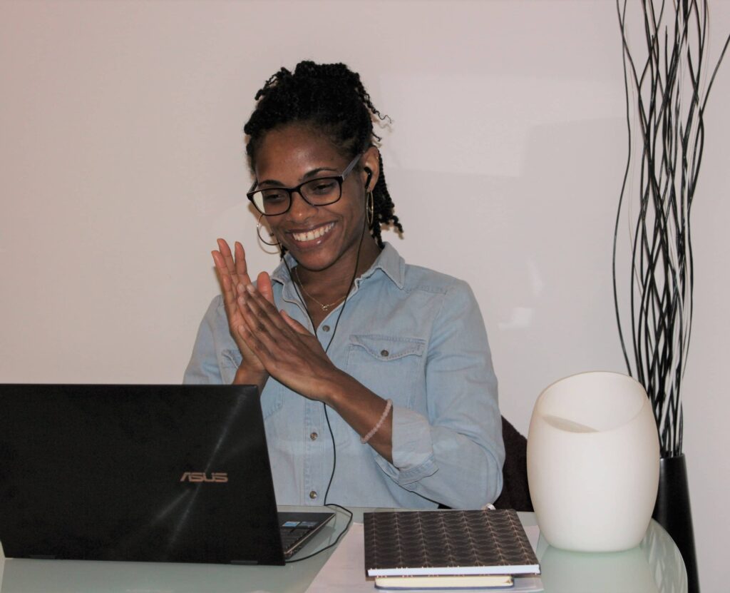 Femme assise à son bureau, sur son PC portable, assistant à une visioconférence avec le sourire