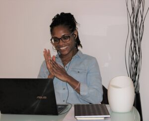 Femme assise à son bureau, sur son PC portable, assistant à une visioconférence avec le sourire