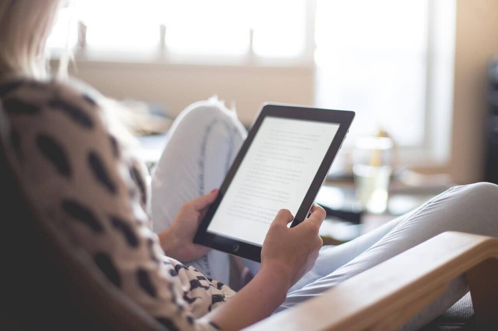 Jeune femme assise en tailleur sur son fauteuil, en train de lire un article de blog sur sa tablette